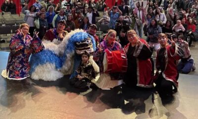 Group of performers posing with a blue-and-white dragon puppet on stage, a child in front, audience in the background.