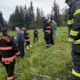 Firefighters in turnout gear line a grassy ditch for a water rescue drill, with ropes and equipment nearby.