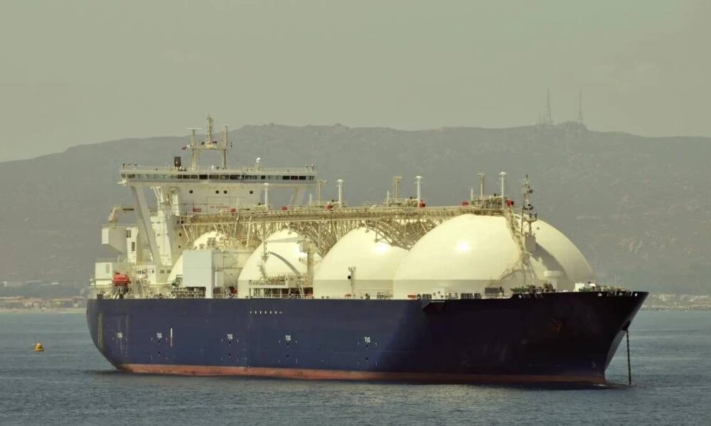 Large LNG carrier with three white spherical tanks sailing near a coastline.