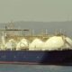Large LNG carrier with three white spherical tanks sailing near a coastline.