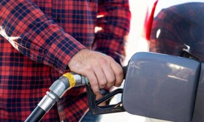 Person in a red plaid shirt grips a gas pump nozzle at a fueling station, fueling a vehicle