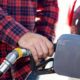 Person in a red plaid shirt grips a gas pump nozzle at a fueling station, fueling a vehicle