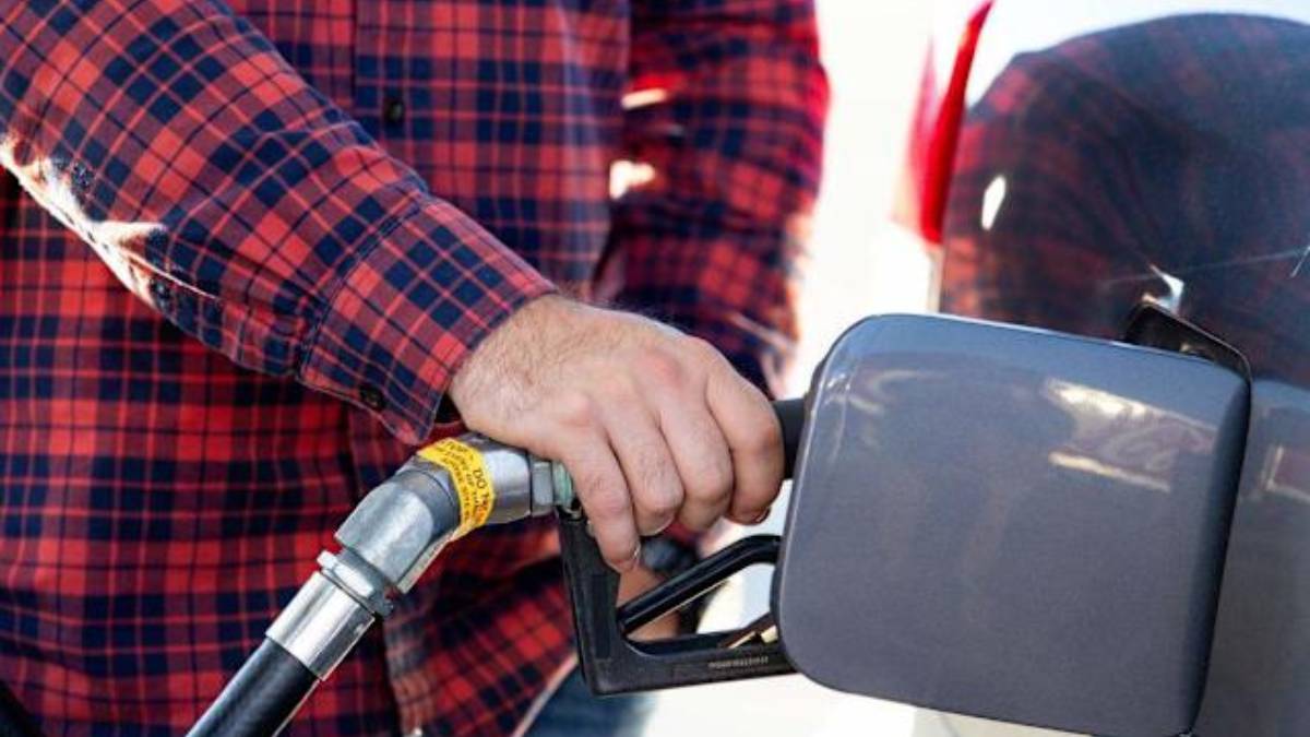 Person in a red plaid shirt grips a gas pump nozzle at a fueling station, fueling a vehicle