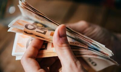 Hands counting a fan of euro banknotes in various denominations on a wooden surface.