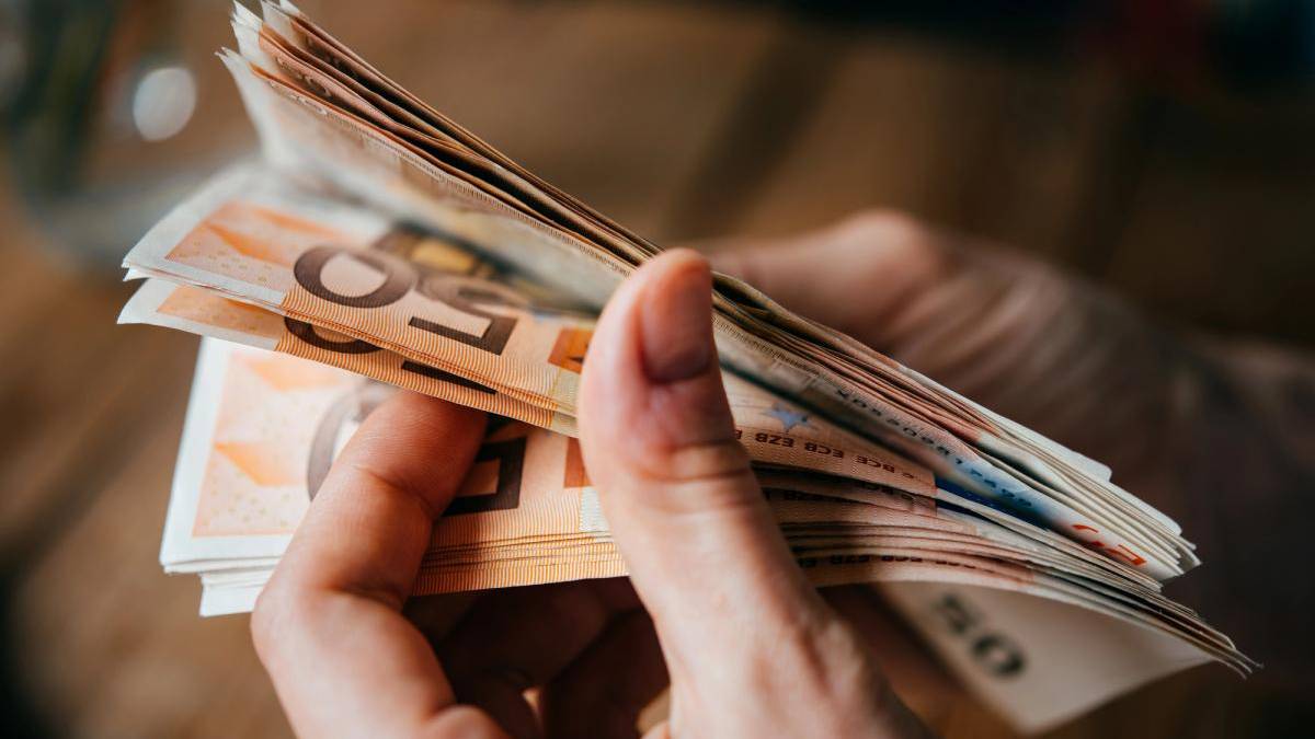 Hands counting a fan of euro banknotes in various denominations on a wooden surface.