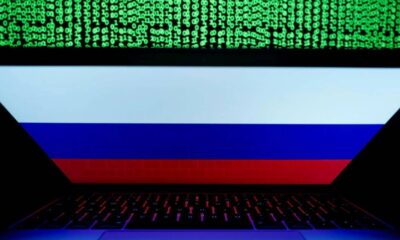 Laptop displaying the Russian flag on screen, with green binary code streaming above.
