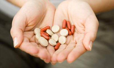 Person cupped hands holding red capsules and beige round pills as if offering medication.