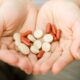 Person cupped hands holding red capsules and beige round pills as if offering medication.