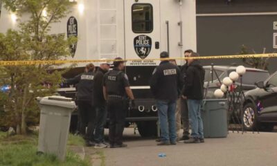 Kent Police crime scene investigators gather around a large white police vehicle behind yellow taped barrier outside a building.