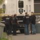 Kent Police crime scene investigators gather around a large white police vehicle behind yellow taped barrier outside a building.