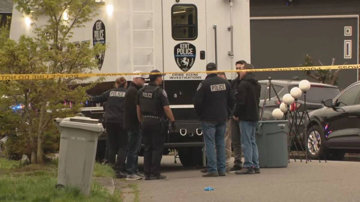 Kent Police crime scene investigators gather around a large white police vehicle behind yellow taped barrier outside a building.
