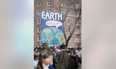 Crowd gathered in protest with a large blue banner reading EARTH HELP and a drawing of the Earth.