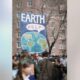 Crowd gathered in protest with a large blue banner reading EARTH HELP and a drawing of the Earth.