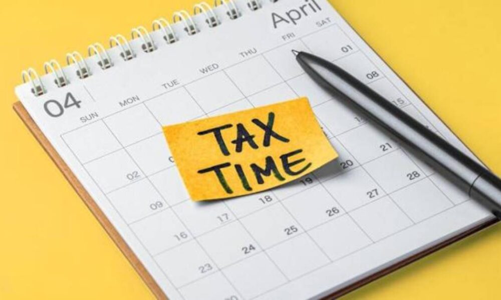 April calendar page with a yellow sticky note reading 'TAX TIME' and a pen nearby on a yellow background.