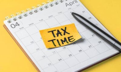 April calendar page with a yellow sticky note reading 'TAX TIME' and a pen nearby on a yellow background.