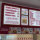 Illuminated fast-food menu board in a red frame listing Double-Double, Cheeseburger, Hamburger, French Fries with prices; below are ordering steps and burger images.