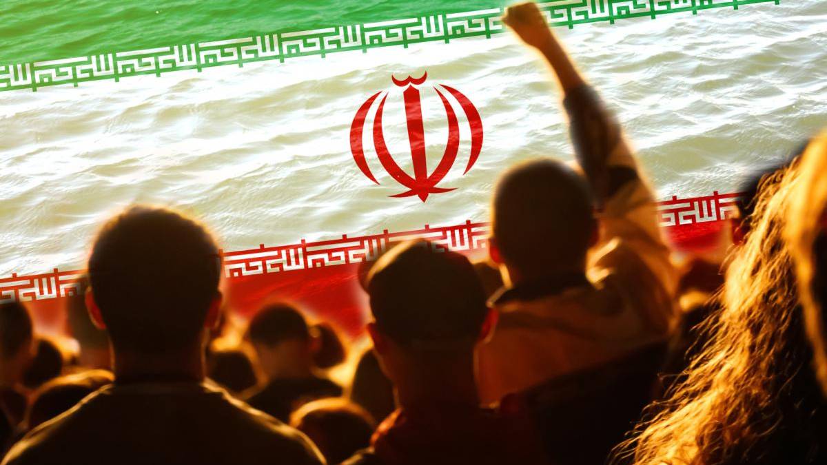 Crowd at a patriotic event waving an Iranian flag banner with green, white, and red bands and emblem.