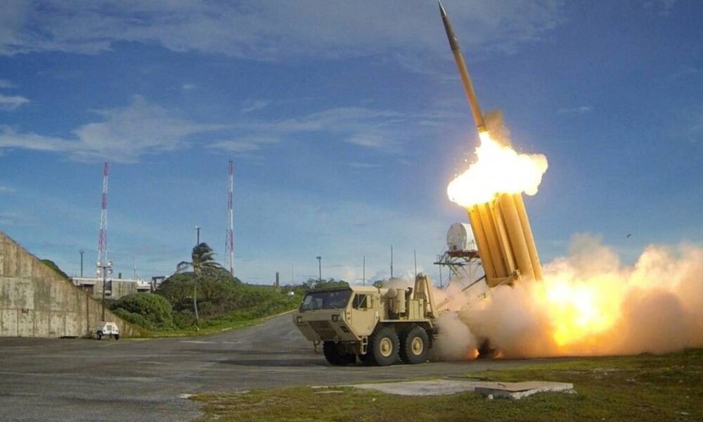 Military rocket launcher fires a missile, producing a bright flame and smoke on a test range.