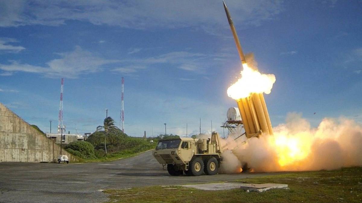 Military rocket launcher fires a missile, producing a bright flame and smoke on a test range.