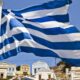 Waving Greek flag on a flagpole with white and blue stripes over a sunny Greek village backdrop