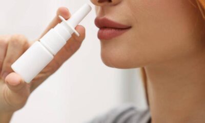 Close-up of a person using a white nasal spray bottle, nozzle near the nostril.