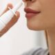Close-up of a person using a white nasal spray bottle, nozzle near the nostril.