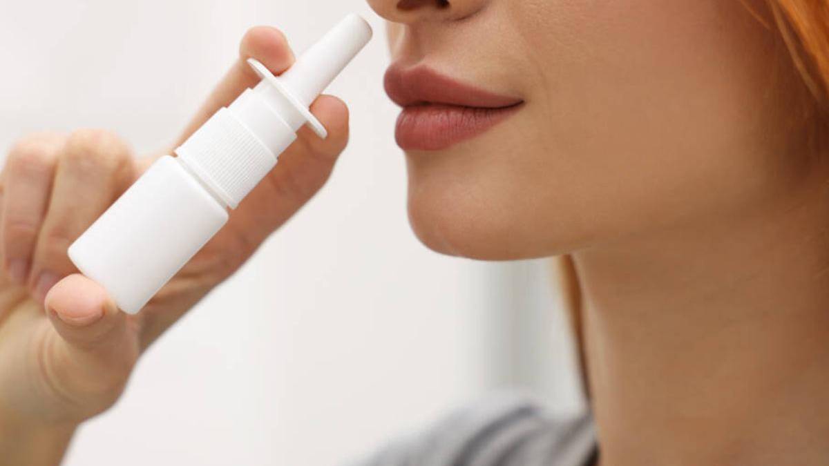 Close-up of a person using a white nasal spray bottle, nozzle near the nostril.