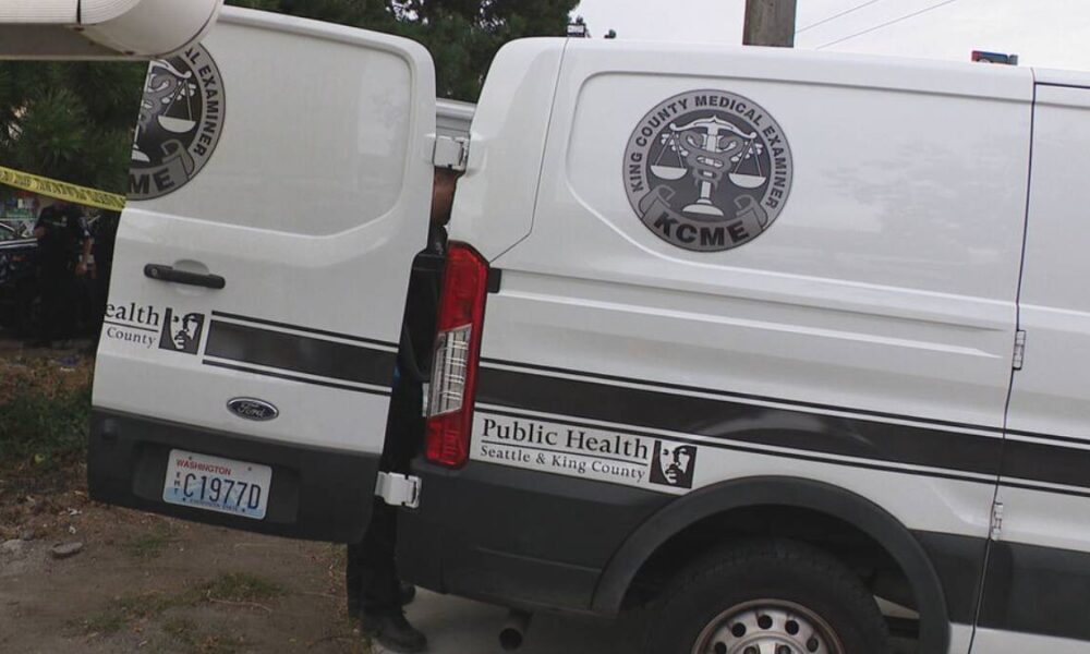Two white vans with Seattle & King County Public Health branding and a KCME medical examiner emblem parked beside yellow caution tape.