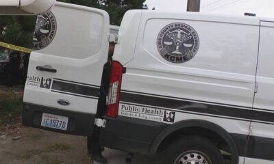 Two white vans with Seattle & King County Public Health branding and a KCME medical examiner emblem parked beside yellow caution tape.