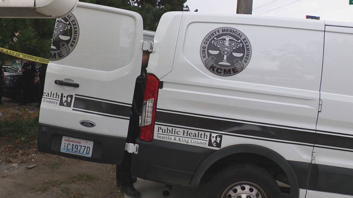 Two white vans with Seattle & King County Public Health branding and a KCME medical examiner emblem parked beside yellow caution tape.
