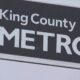 King County METRO sign with a square portrait logo on the left and bold METRO text on a dark background.