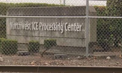 Chain-link fence in front of a sign that reads Northwest Processing Center behind a hedge-lined concrete wall.