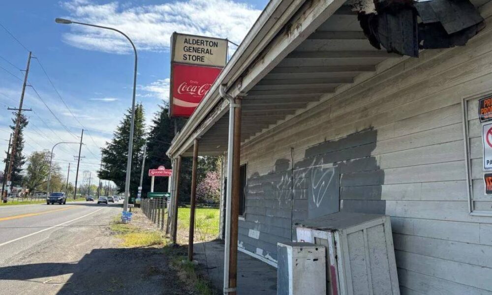 Abandoned wooden storefront along a street with peeling paint, graffiti, and a Coca-Cola sign above.