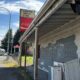 Abandoned wooden storefront along a street with peeling paint, graffiti, and a Coca-Cola sign above.
