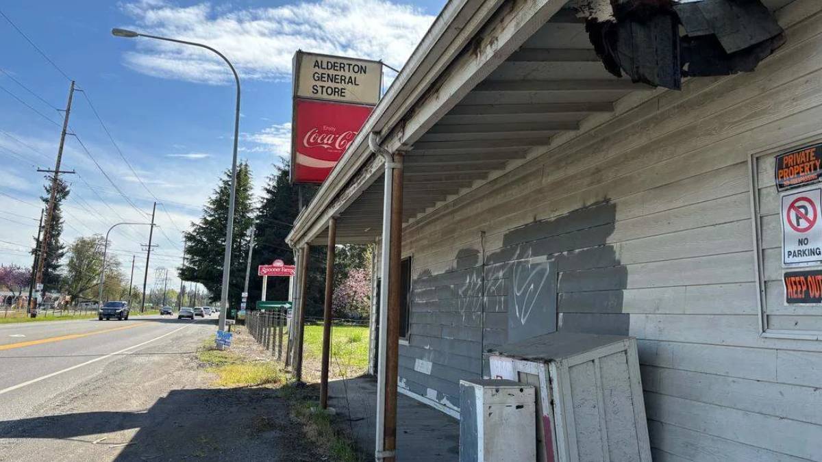 Abandoned wooden storefront along a street with peeling paint, graffiti, and a Coca-Cola sign above.