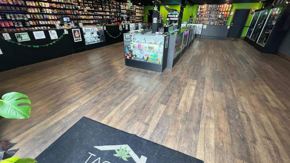 Interior of a cannabis shop with glass display cases, wall shelves stocked with products, and green accents along the walls and ceiling banners.