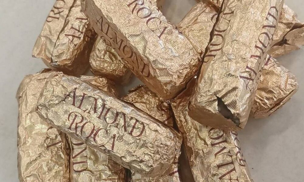 Pile of Gold Almond Roca candies in crinkled gold foil wrappers on a light surface