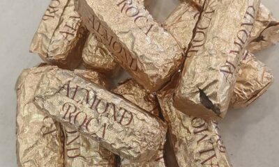 Pile of Gold Almond Roca candies in crinkled gold foil wrappers on a light surface