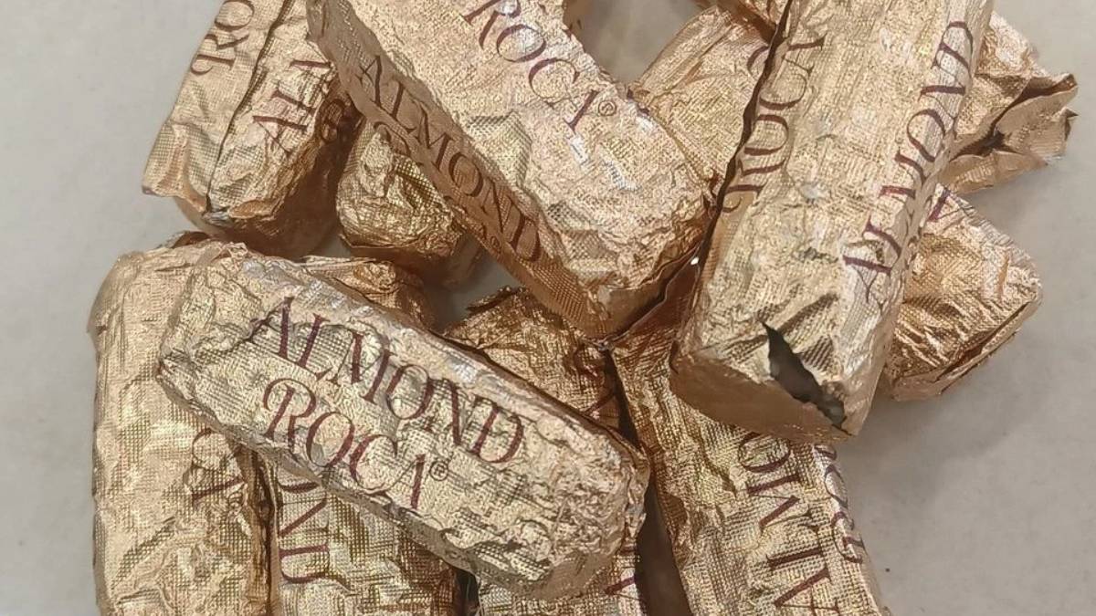 Pile of Gold Almond Roca candies in crinkled gold foil wrappers on a light surface