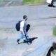 Young man with a backpack walking across a street curb in a residential area, sidewalk and parked cars visible in the background