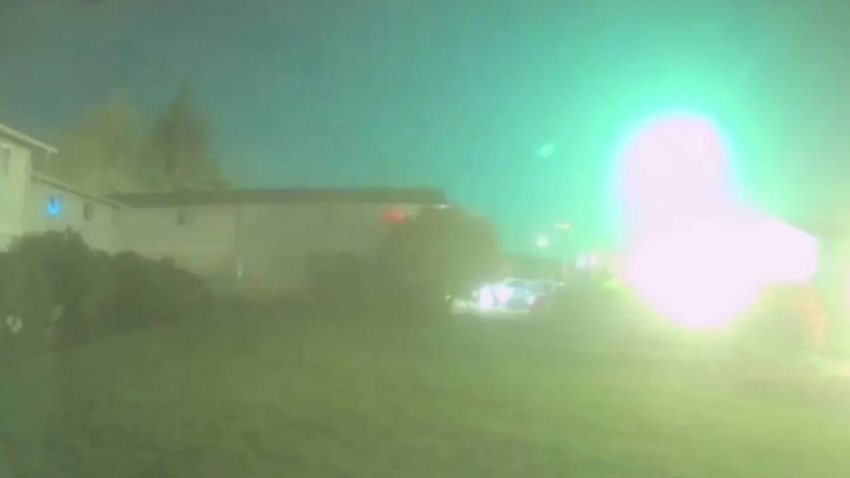 Blurry nighttime street scene with a bright green emergency light flare on the right and a parked car in the distance.