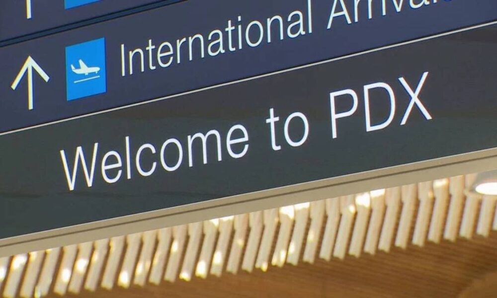 Airport sign reading 'International Arrivals' with airplane icon and 'Welcome to PDX'.