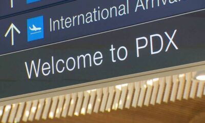 Airport sign reading 'International Arrivals' with airplane icon and 'Welcome to PDX'.