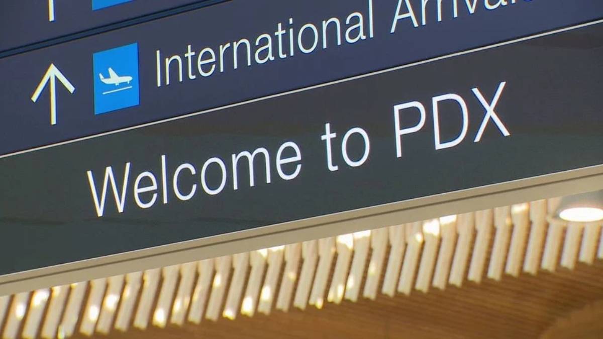 Airport sign reading 'International Arrivals' with airplane icon and 'Welcome to PDX'.