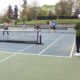 Doubles tennis match on an outdoor court with spectators lined up along the fence.