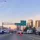 Highway scene with police SUV and orange traffic cones blocking lanes, city skyline in the distance.