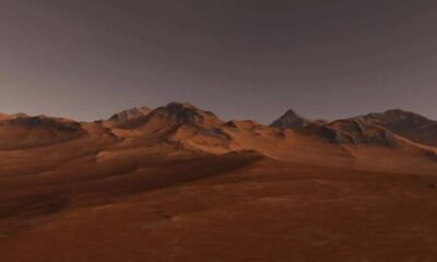 Desert plain in orange-red tones with a rocky mountain range on the horizon under a dusky sky, twilight light.
