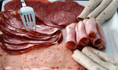 Assorted deli meats on a white platter: pepperoni slices, salami, rolled ham, and pale herb-infused sausages with a fork resting on top.