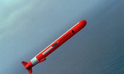 Red missile with white stripes angled diagonally through a blue-gray sky over the ocean.
