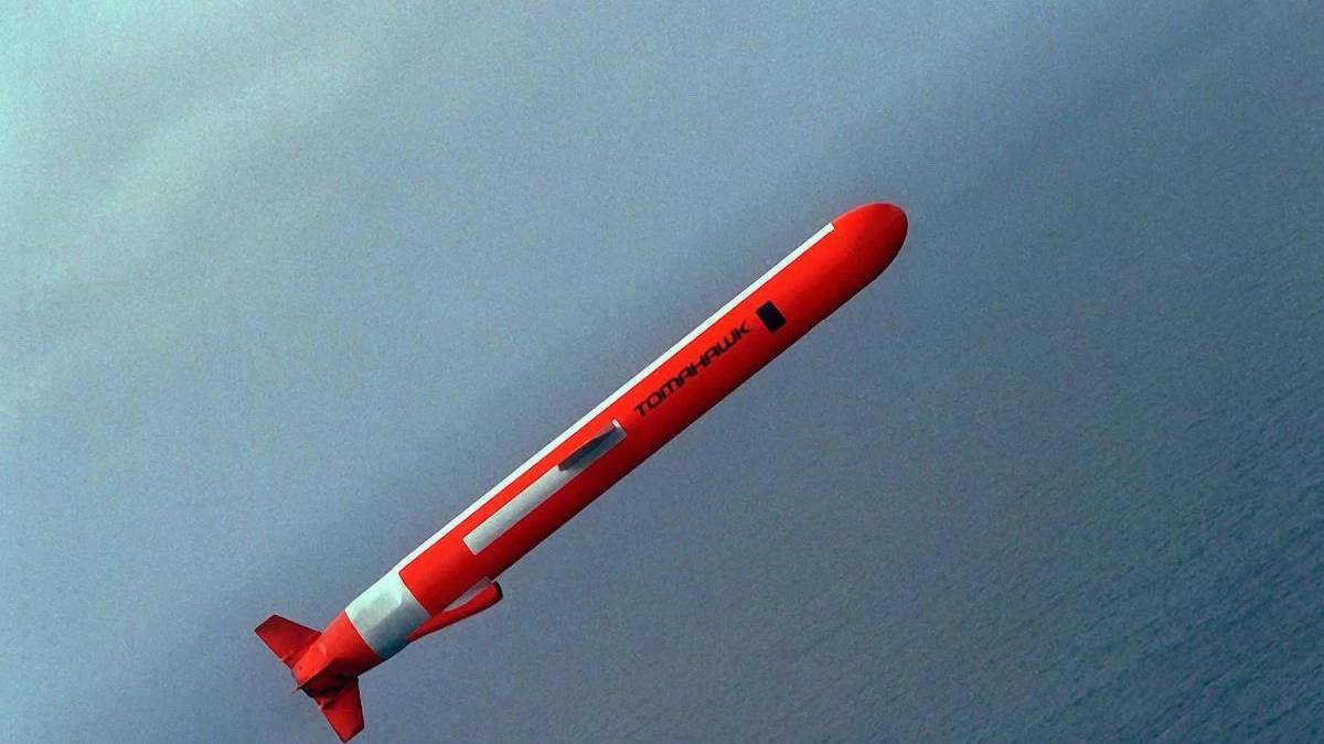 Red missile with white stripes angled diagonally through a blue-gray sky over the ocean.